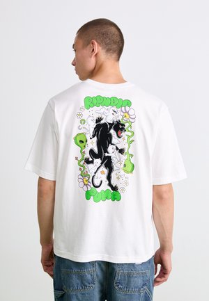 Person wearing a white t-shirt with a colorful back design of a black panther, white cats, green alien heads, flowers, and the text "RIPNDIP PUMA".
