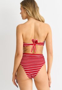Red and white striped bikini set with a bandeau top tied at the back and high-waisted bottom, featuring a textured fabric.