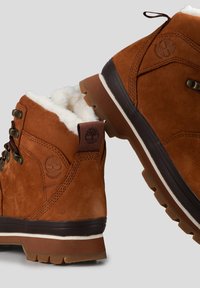 Bruine waterdichte laarzen van suede met een nepbont voering, uitgerust met metalen oogjes, een gebogen design en een robuuste buitenzool voor grip.