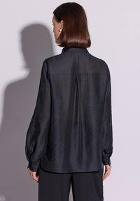 Czarna jedwabna bluzka o luźnym kroju, z długimi bufkami na rękawach i ozdobnym karczkiem z tyłu. Gładka faktura i subtelny połysk podkreślają jej wygląd.