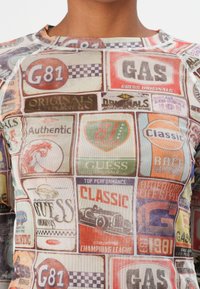 Long-sleeve shirt featuring a collage of colorful vintage labels and logos in various shapes, set against a light background.