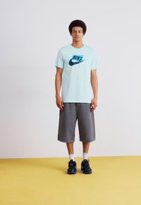 Světle modré tričko Nike s černým a tyrkysovým logem, spárované se šedými šortkami a černými teniskami s modrými akcenty.