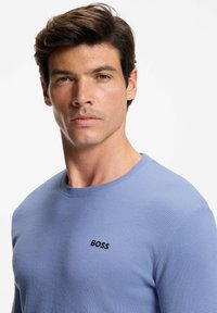Light blue long-sleeve shirt with a textured pattern and a round neckline. Features a black "BOSS" logo on the chest.