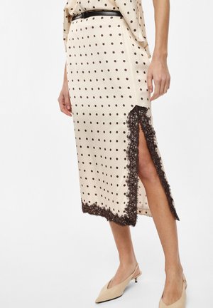 Gonna midi beige con pois neri, spacco laterale rifinito in pizzo nero, indossata con scarpe slingback beige a tacco basso e cintura.