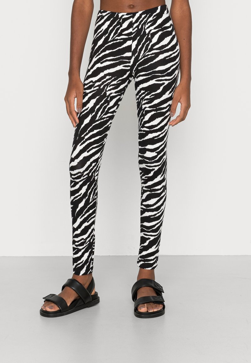 Leggings a stampa zebrate bianco e nero realizzati in tessuto elasticizzato, abbinati a sandali neri piatti con cinturini larghi e dettaglio fibbia.