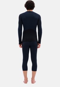 Thermisch onderlaagset in donkerblauw. Langsleeve top en capri-lengte onderkant. Gladde textuur met subtiele mesh accenten op de broek.