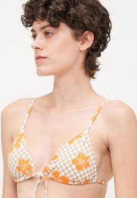 Trekantet bikinitopp med et beige og oransje rutemønster, prydet med oransje blomsterdesign, justerbare stropper og en knute i midten.