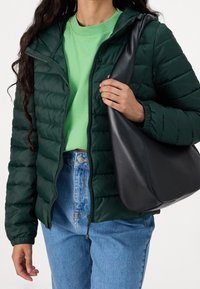 Ciemnozielona pikowana kurtka z suwakiem z przodu, zestawiona z jasną zieloną koszulką i jasnoniebieskimi dżinsami. Czarna, luźna torba typu tote.