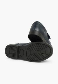 Tumši zili ādas apavi ar gludu augšdaļu, Velcro siksnu un teksturētu gumijas zoli, kurai ir rakstaina virsma labākai saķerei.
