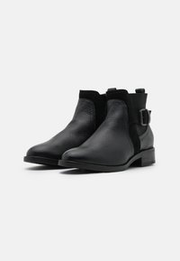 Botas de cuero negro hasta el tobillo con acentos de ante, detalle de hebilla y un tacón bajo apilado. Textura suave con un diseño de punta redondeada.