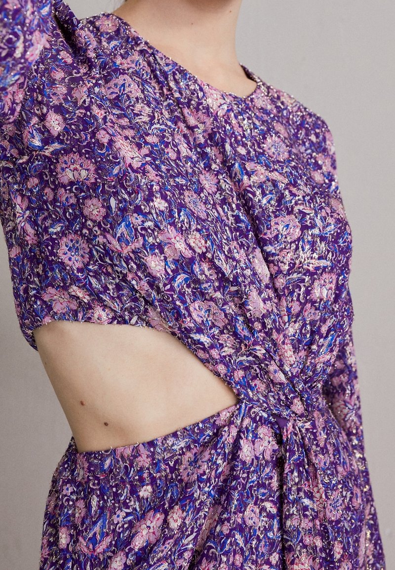 Lila blommig klänning med urklippsdetaljer, korta ärmar, knuten midja och ett texturerat tyg med inslag av rosa och blått.