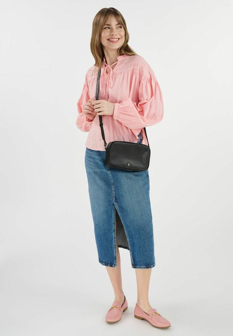 Czarna torba na krzyż z zamkiem błyskawicznym, noszona na różowej bluzce z balonowymi rękawami oraz dżinsowej spódnicy z rozcięciem z przodu. Różowe lordsy.