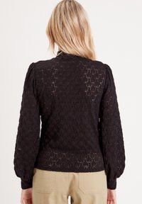 Pull en maille noir avec texture en crochet à motif losange, manches ballon et ourlet côtelé. Présente une coupe courte.