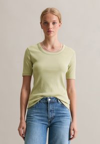 Lichtgroene geribbelde t-shirt met korte mouwen en een ronde hals, gecombineerd met blauwe denim jeans. De stof lijkt zacht en aansluitend te zijn.