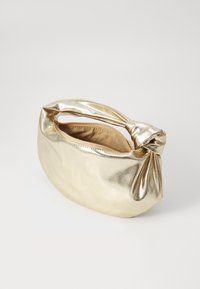Petit sac à main doré brillant avec un détail de nœud sur la anse, fermeture éclair partiellement ouverte et intérieur doublé de tissu sur fond blanc.