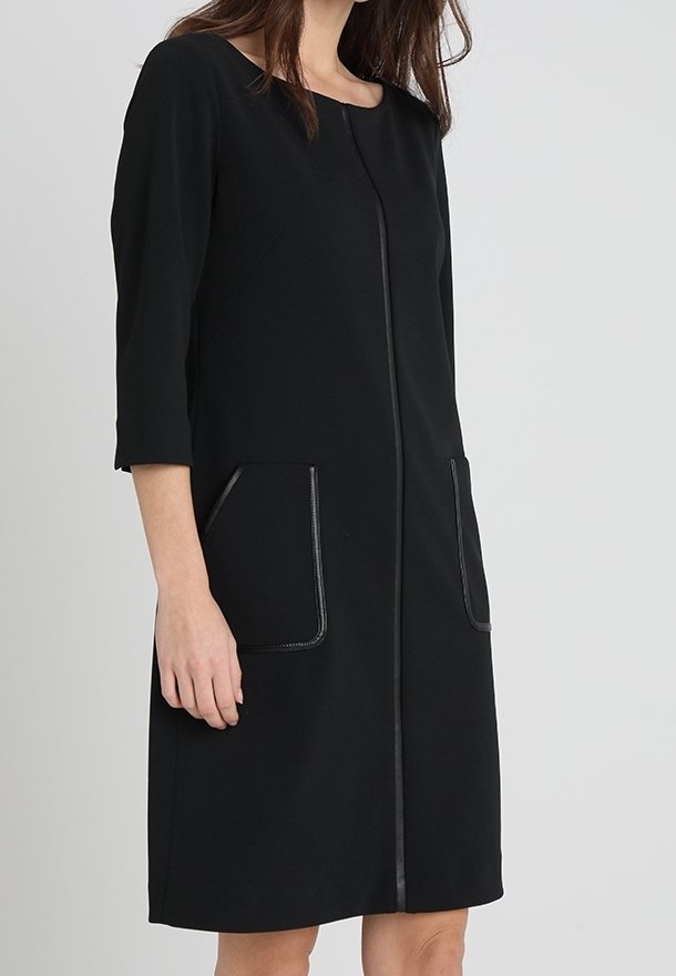 Robe noire à manches trois-quarts, col rond, deux poches avant, et une fermeture éclair centrale. Tissu lisse avec des accents contrastants sur les poches.