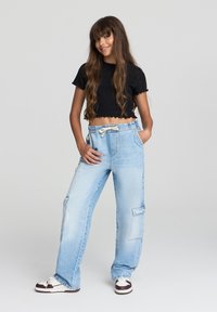 Jasnoniebieskie spodnie cargo z elastycznym pasem, bocznymi kieszeniami i luźnym krojem, zestawione z czarnym topem na krótki rękaw i białymi sneakersami.