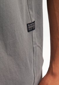 Šedé bavlněné tričko s vertikálním švem a nášivkou G-Star RAW na boku. Hladká textura s pohodlným střihem.