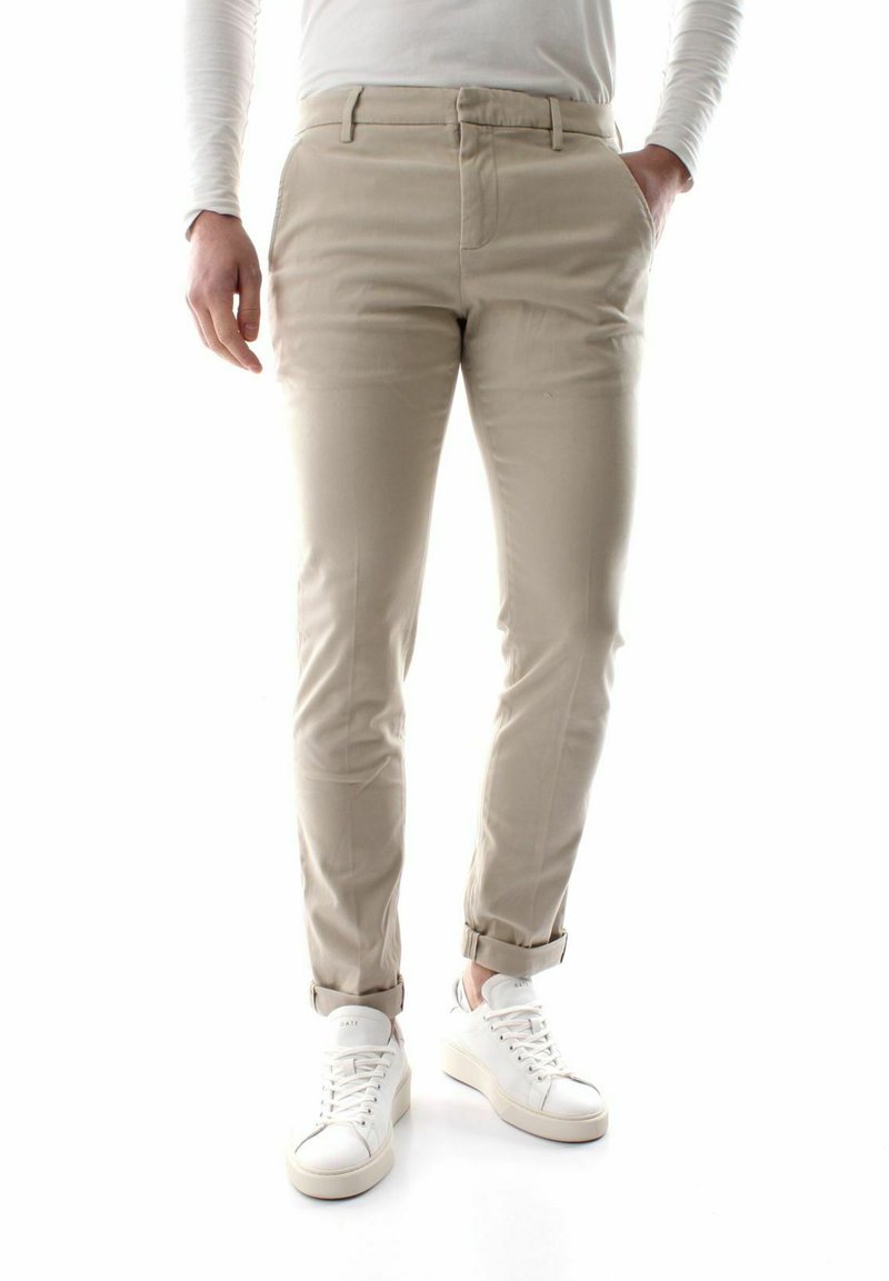 Pantaloni beige in misto cotone, slim fit con orli arrotolati, abbinati a sneakers bianche. Tessitura liscia, dettagli di cuciture minimi.