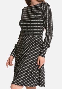 Schwarz-weiß gestreiftes Kleid mit langen Ärmeln. Vertikale Blumenmuster über das gesamte Kleid, tailliertes Oberteil, das in einen ausgestellten Rock übergeht. Weiche Stofftextur.