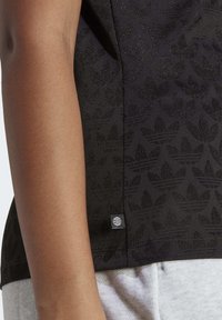 Svart T-shirt med ett texturerat lövmönster, med en liten logotagg vid fållen. Tyget verkar slätt och något skinande.