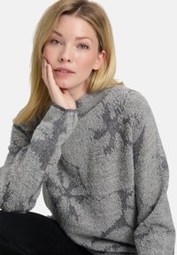 Pullover aus weichem, strukturiertem Stoff in hellgrau mit einem dunkler grauen abstrakten Muster, mit hohem Kragen und langen Ärmeln.
