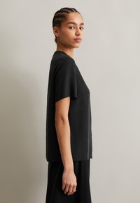 Schwarzes Kurzarmtop aus glattem Stoff. Minimalistisches Design mit lässiger Passform, das subtile Nahtdetails an den Seiten aufweist.