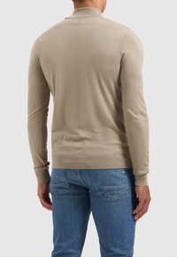 Beige, lange mouwen trui met een ronde halslijn en ribgebreide manchetten en zoom, gezien vanuit de achterkant, gecombineerd met lichtblauwe jeans.