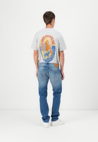 Gray graphic t-shirt with colorful mountain and deer design on back, paired with light blue jeans and white sneakers. Casual fit, no prominent textures.