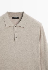 Pullover beige chiaro con colletto polo, tessuto a maglia testurizzato e chiusura a tre bottoni. Presenta leggere variazioni di colore e un'etichetta.