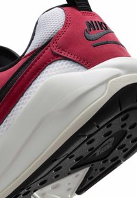 Calzado Nike con parte superior de malla roja y blanca, acentos de ante suave y suela de goma negra texturizada con agarres circulares.