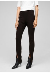 Svarta slim-fit byxor med sidosprund vid fållen, tillverkade av ett stretchigt material. Bärs med spetsiga svarta ankelskor med en slät yta.