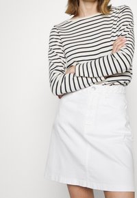 Maglietta a maniche lunghe a righe in crema e blu navy, abbinata a una gonna di jeans bianca con vita strutturata e tasche frontali.
