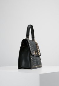 Svart läderhandväska med kviltad struktur, gulddetaljer och nitar längs basen. Inkluderar en topphandtag och ett lock med stängning.