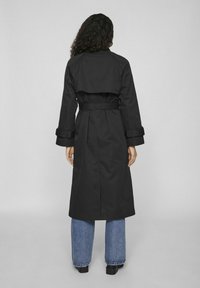 Palton negru din trench cu taliefixă și mâneci cu manșete, având un design pe panoul din spate. Purta peste blugi largi albaștri.