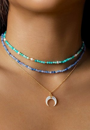 Colliers de perles superposées mettant en avant des perles turquoises, bleues et en perles, avec une chaîne dorée et un pendentif en forme de croissant de lune.