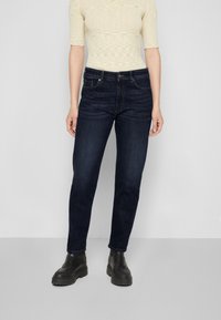 Tmavě modré džíny s rovný fit, se pěti kapsami, kovovými detaily a minimálním vyblednutím, spárované s černými kotníkovými botami.