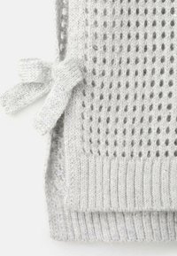 Detajl svetlo sive pletene majice s teksturiranim vzorcem z odprto pletenino, rebrastim robom in bočnim zapiranjem s trakom.