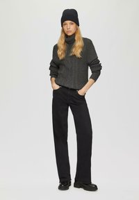 Czarny sweter z turtleneckiem w ciemnoszarym kolorze, czarne spodnie z szerokimi nogawkami oraz czarne masywne buty, do tego ciemna dziana czapka. Prosta, casualowa stylizacja.