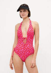 Ροζ φλοράλ ολόσωμο μαγιό με βαθύ V-ντεκολτέ, λεπτομέρεια κορδονιού στη μέση και μοτίβο κειμένου. Διαθέτει πλάγιες πτυχώσεις και ιμάντες χιαστί λαιμού.