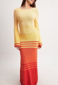 Robe longue moulante avec une texture tricotée. Dégradé de couleurs passant du jaune en haut à l'orange en bas, avec des rayures horizontales.