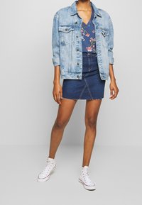 Světle modrá džínsová bunda přes námořnický květinový top, spojená s tmavě modrou mini sukni a bílými teniskami na vysoké podrážce. Neformální městský outfit.