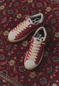 Paire de baskets rouges et blanches avec lacets crème et étiquette P448 sur un fond de tapis rouge et multicolore à motifs.
