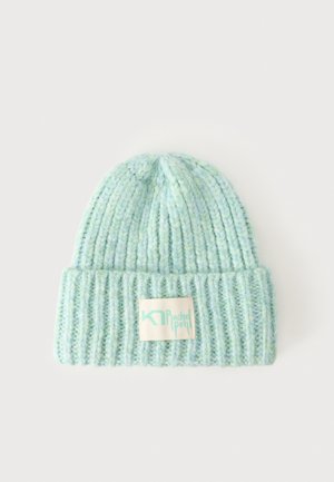 Gorro de punto acanalado azul claro con puño doblado y una etiqueta blanca rectangular en el frente.