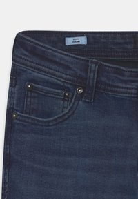 Slim-fit mörkblå denimjeans med subtil textur, som har framfickor, metallbeslag och en etikett med texten "SLIM GLENN."