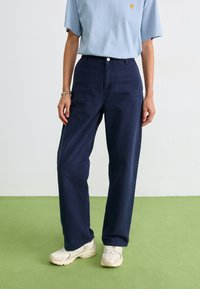Pantalons larges bleu marine en coton avec une fermeture à bouton. Associés à un haut bleu clair et des baskets couleur crème.