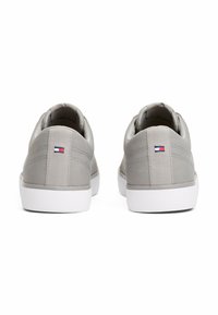 Sneakers grigi con una texture liscia, dotati di suola in gomma bianca e un piccolo logo colorato sul retro, caratterizzati da un design minimalista.