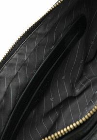 Interno di una borsa nera con zip, caratterizzato da una fodera liscia e testurizzata con sottili righe alternate. Cerniera dorata lungo il bordo superiore.