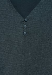 Haut texturé vert foncé avec un décolleté en V, trois boutons noirs à l'avant et une finition en tissu légèrement froissé.