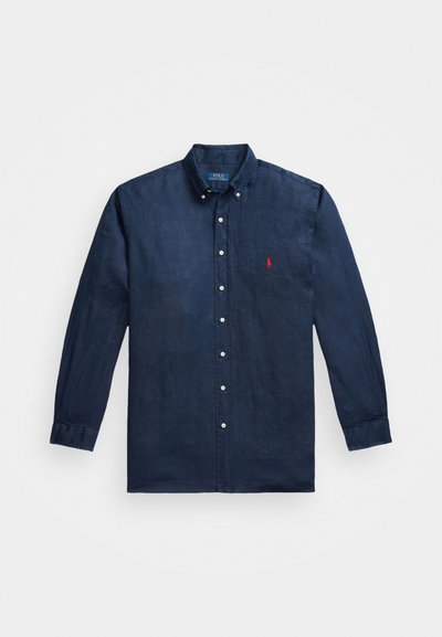 Camisa de manga longa azul-marinho feita de linho, com colarinho abotoado e um único logo vermelho no lado esquerdo do peito. Apresenta botões brancos.